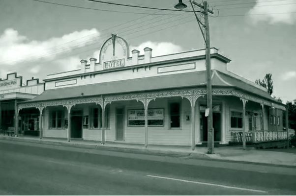 Black-and-white photo of a historic corner hotel building in Pambula, NSW, featuring ornate verandah posts, a “HOTEL” sign on the roof, and a quiet street with a utility pole and overhead wires in front.